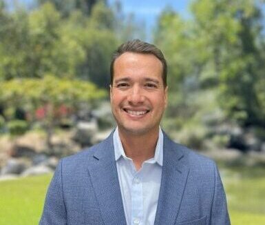 Ryan Holt, Business Development team member at American Golf Corporation, smiling in a blue blazer outdoors in a garden setting.